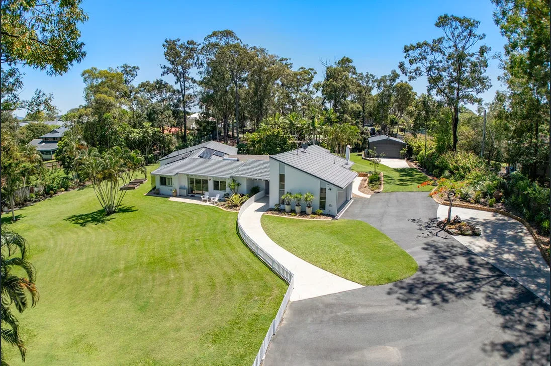 Aerial view of a home with a paved entry path and driveway, surrounded by lawn and trees